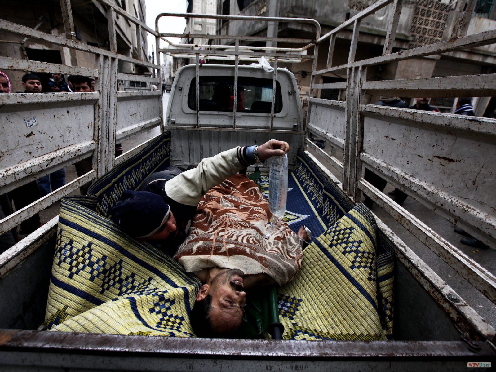 Syrie, Homs. Quartier de Karm al-Zaytoun.
Un homme blessé par un sniper est évacué dans une camionnette qui est elle-même susceptible d’être la cible de tirs. L’homme blessé ne survivra pas.
<br><b><i>
A man hit by sniper fire is evacuated in a vehicle which is then likely to be targeted. The man did not survive. </i></b>
